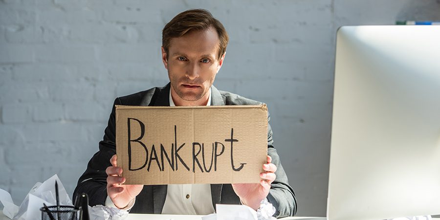 Upset businessman holding cardboard with bankrupt lettering, whi