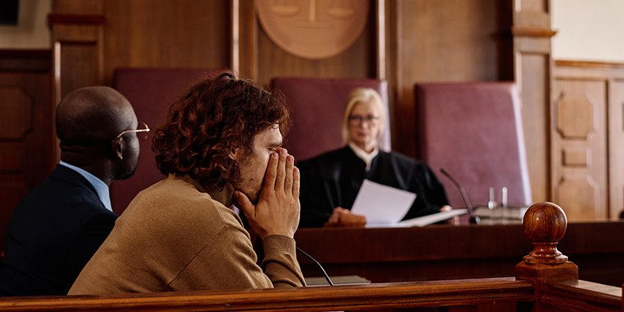 Young anxious male suspect covering his face by hands during verdict